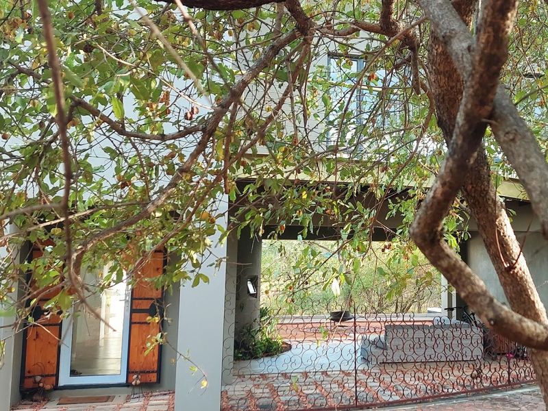 A view of the rear exterior featuring a covered patio area, paved flooring, and decorative wrought iron fencing, partially obscured by mature tree branches.