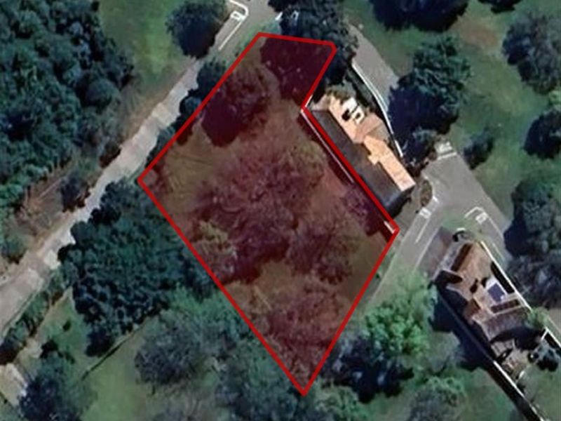 Aerial view of a vacant residential plot outlined in red, situated within a landscaped neighborhood setting.