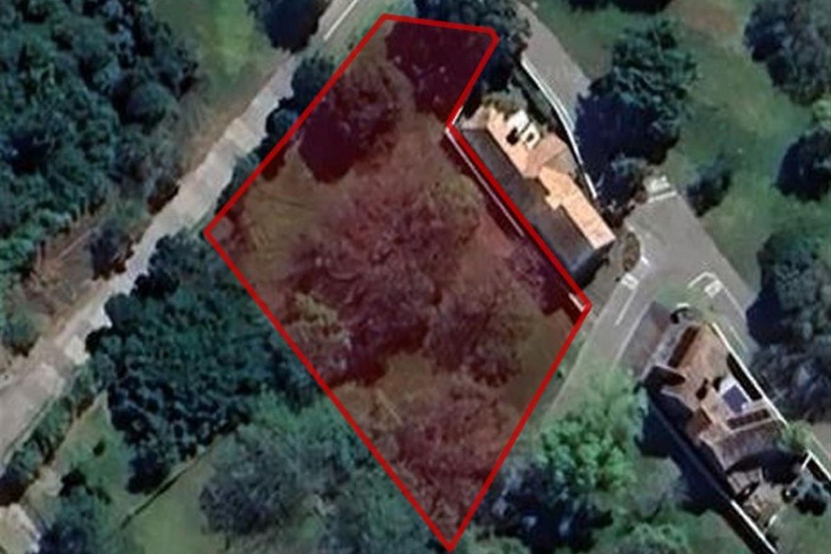 Aerial view of a vacant residential plot outlined in red, situated within a landscaped neighborhood setting.