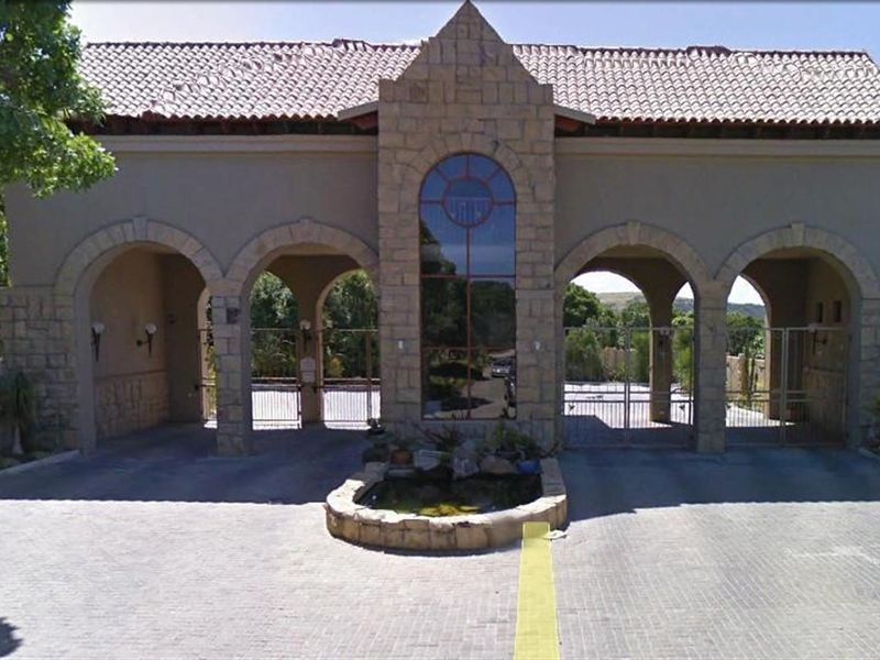 A secure gated entrance featuring stone masonry, arched gateways, a central water feature, and tiled roofing, providing access to the residential property.