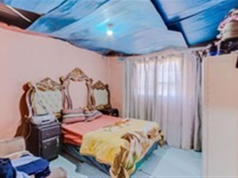 A bedroom featuring a window with curtains and a damaged ceiling structure.