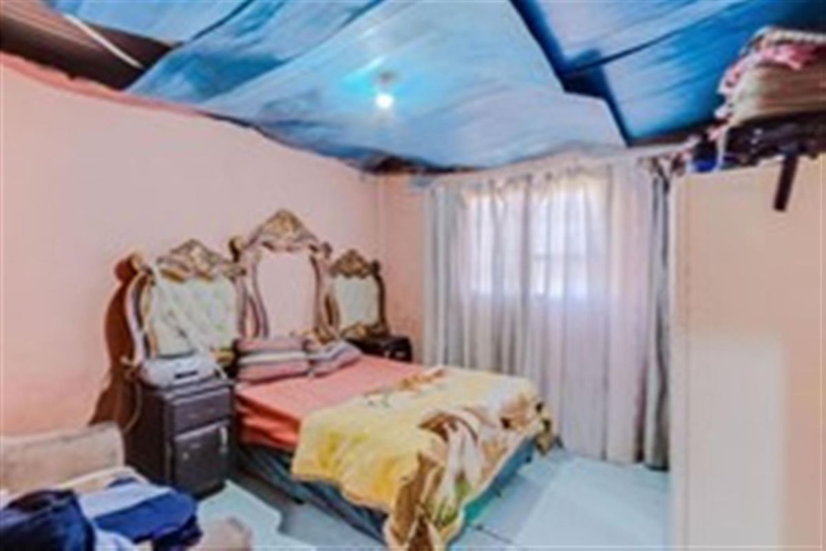 A bedroom featuring a window with curtains and a damaged ceiling structure.