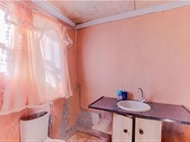 A small bathroom featuring a vanity basin and toilet, currently requiring significant cosmetic repairs and wall surface restoration.