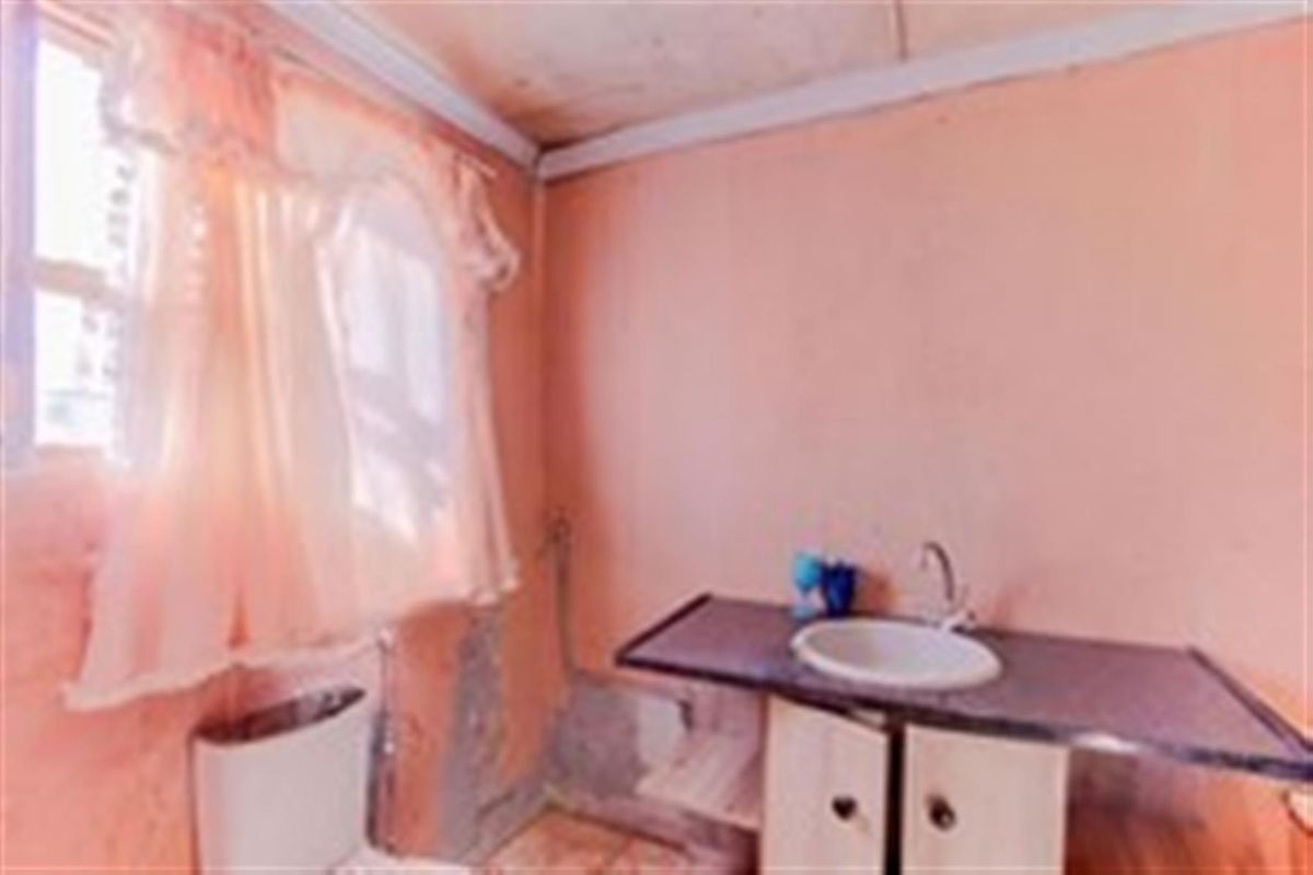 A small bathroom featuring a vanity basin and toilet, currently requiring significant cosmetic repairs and wall surface restoration.