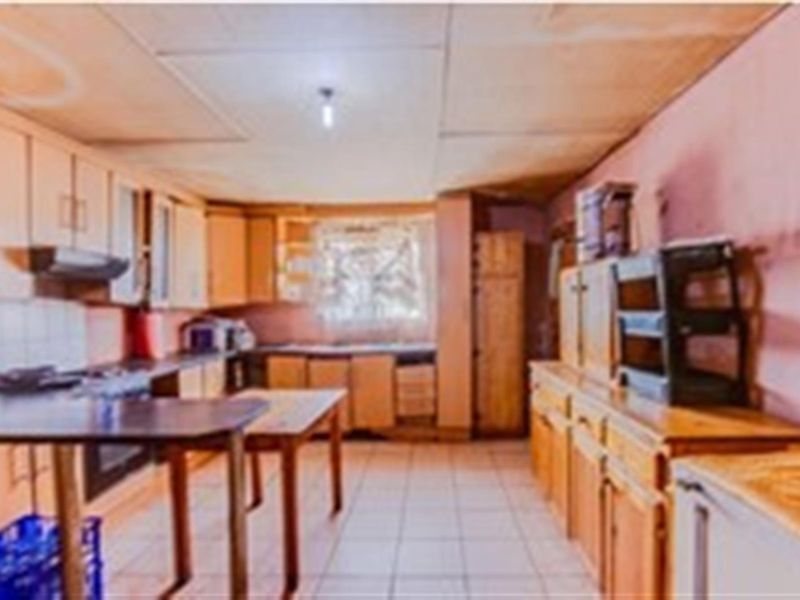 A dated kitchen featuring extensive built-in cabinetry, tiled flooring, and an extractor fan, offering significant potential for modernization and renovation.
