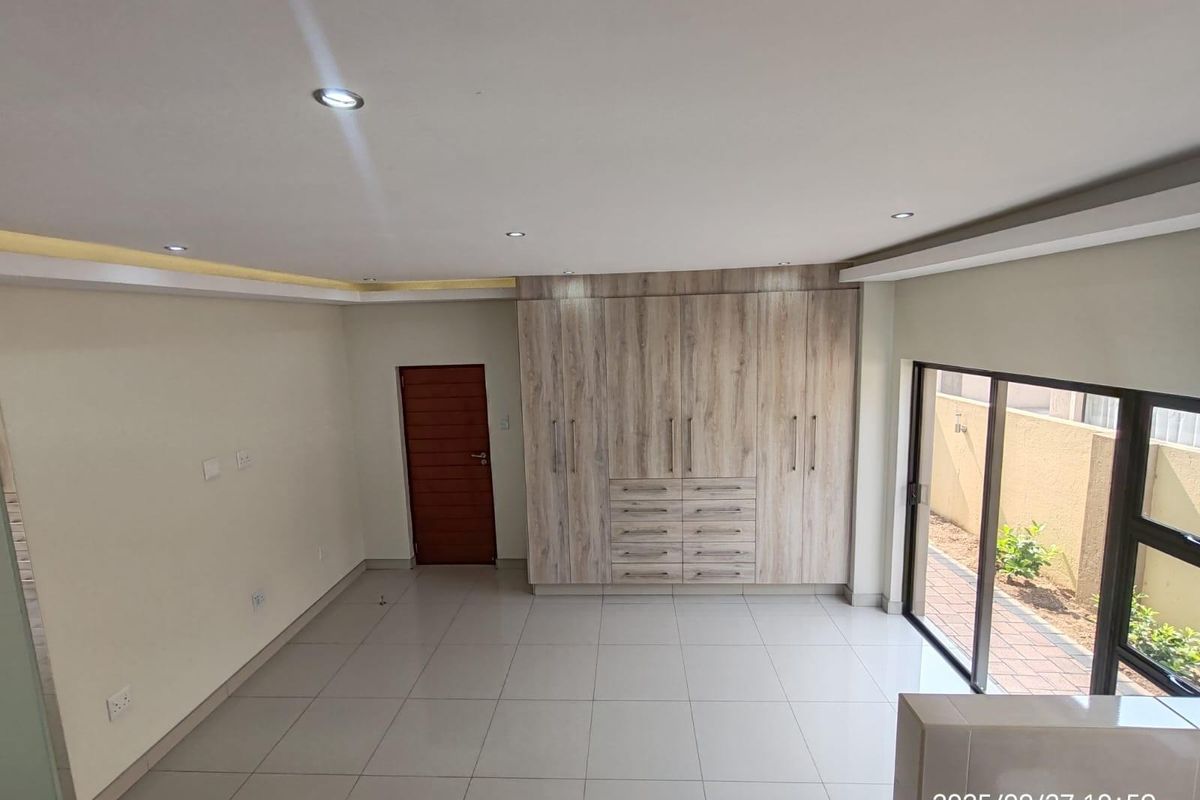 A bright, empty bedroom featuring modern built-in wooden cabinetry, tiled flooring, recessed ceiling lighting, and sliding glass doors leading to an outdoor area.