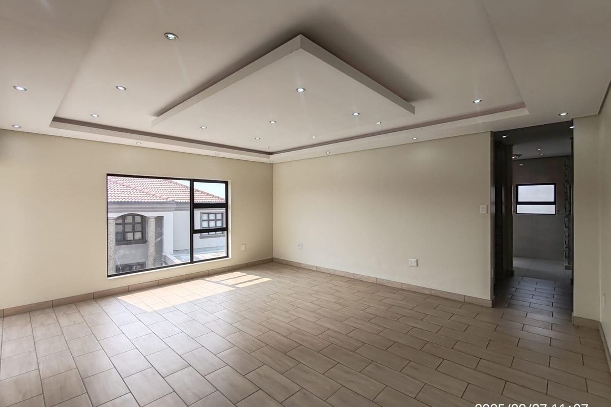 Spacious living area featuring modern recessed tray ceiling with downlights, large windows, and neutral tiled flooring throughout.
