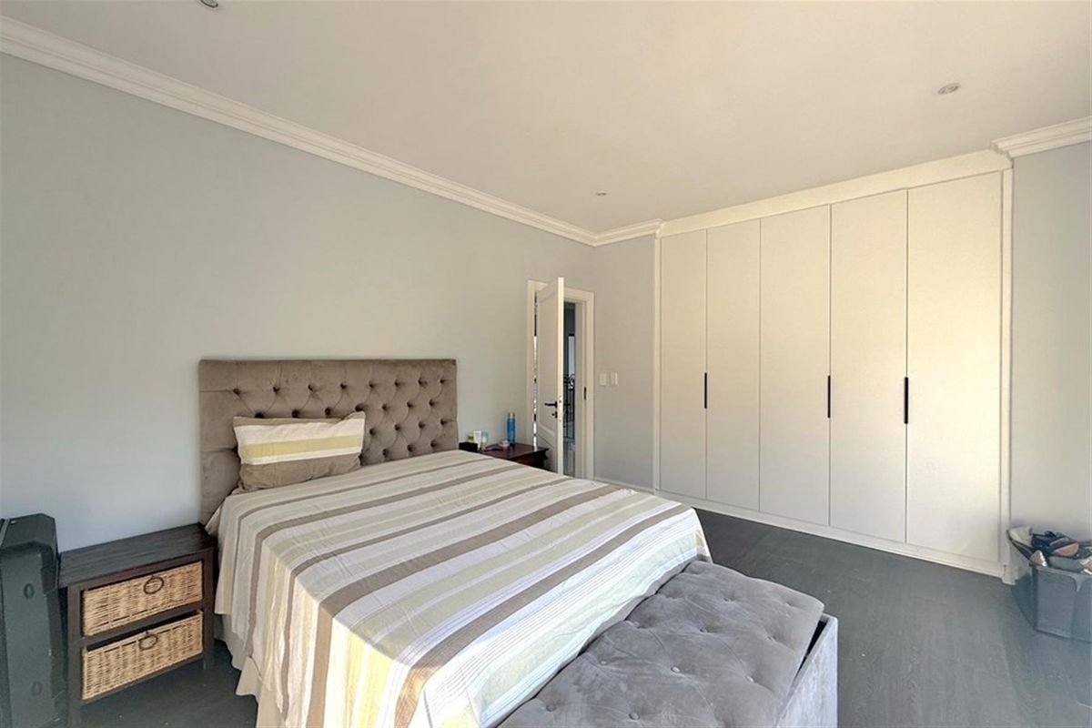 A well-maintained bedroom featuring built-in floor-to-ceiling wardrobes, crown molding, and dark wood-look flooring.