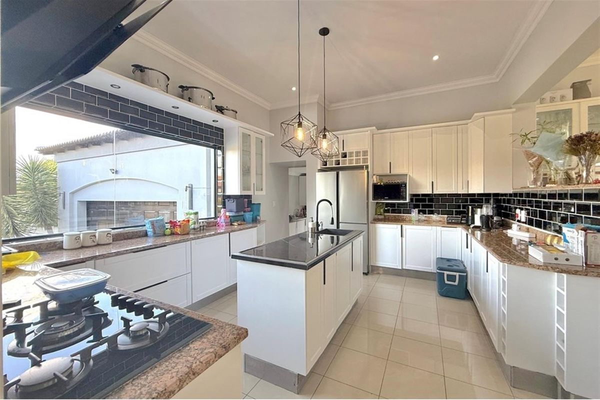 Modern kitchen featuring white cabinetry, granite countertops, a central island with a sink, and a black subway tile backsplash.