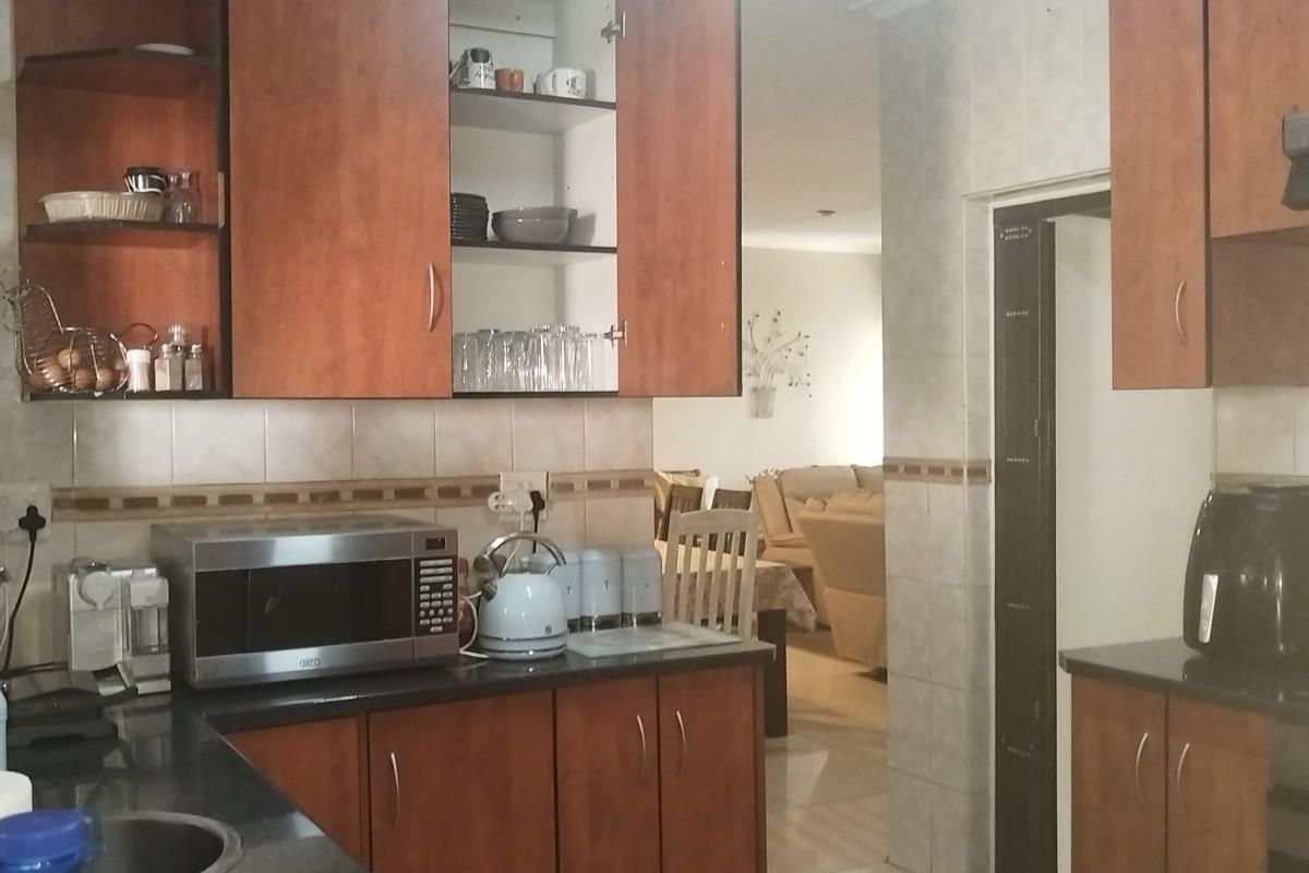 A functional kitchen featuring wood-veneer cabinetry, dark granite countertops, and a tiled backsplash, with an open-plan layout leading into the adjacent living area.