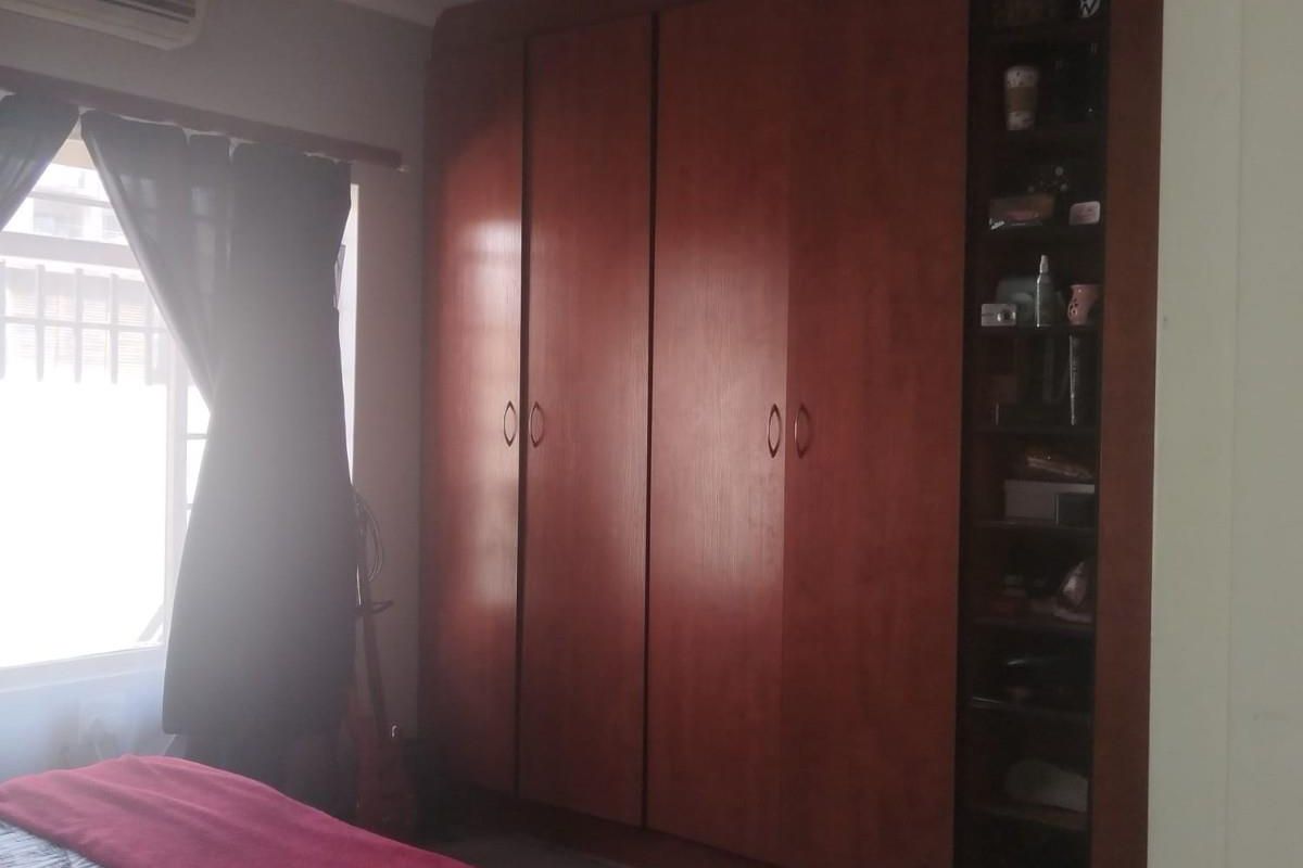 A bedroom featuring built-in wooden cabinetry with integrated shelving and a wall-mounted air conditioning unit.