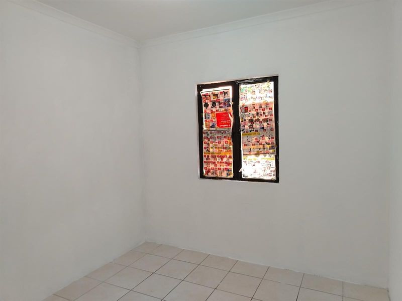 A vacant, neutrally painted room featuring tiled flooring and a single window, offering a blank canvas for potential interior design and personalization.