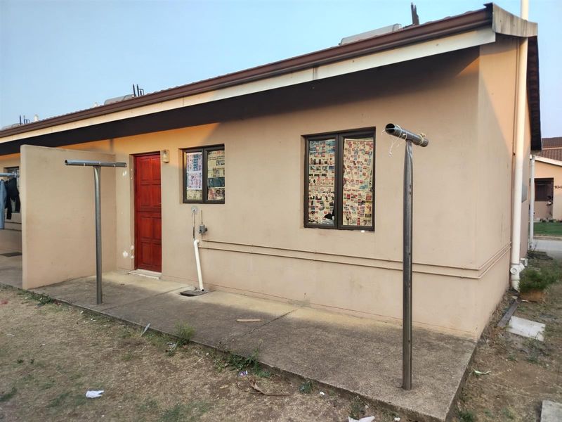 Rear exterior view of the house featuring a concrete patio area, metal washing lines, and a single wooden entrance door.
