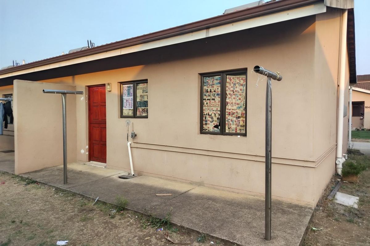 Rear exterior view of the house featuring a concrete patio area, metal washing lines, and a single wooden entrance door.