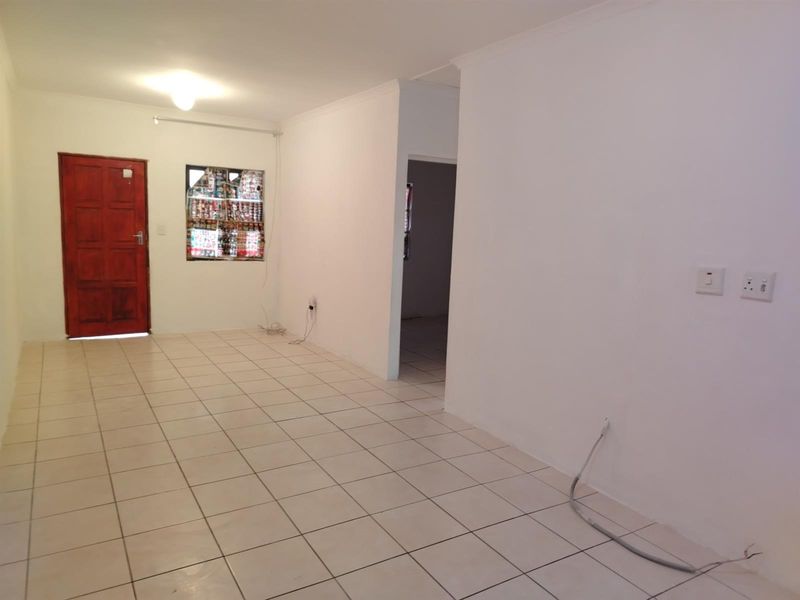 An open-plan living area featuring neutral tiled flooring, a solid timber entrance door, and direct access to adjacent rooms.