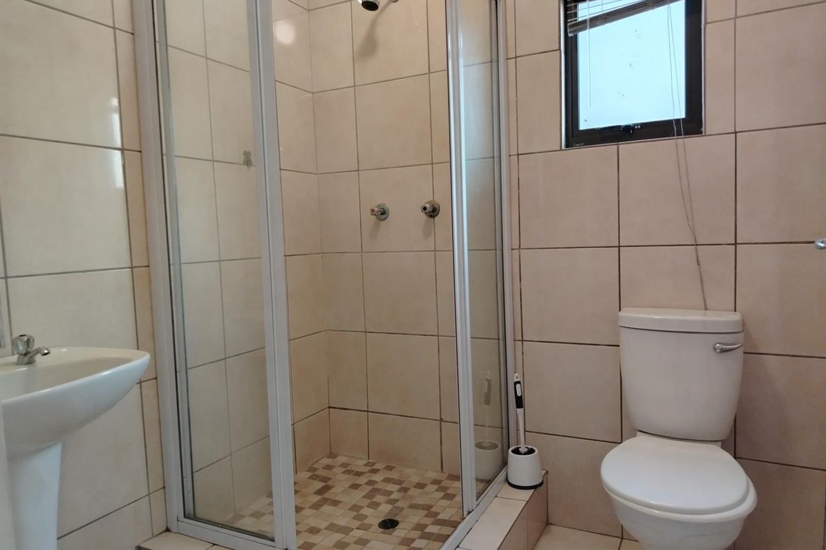 A functional bathroom featuring a glass-enclosed shower, pedestal basin, and standard toilet with neutral wall tiling.