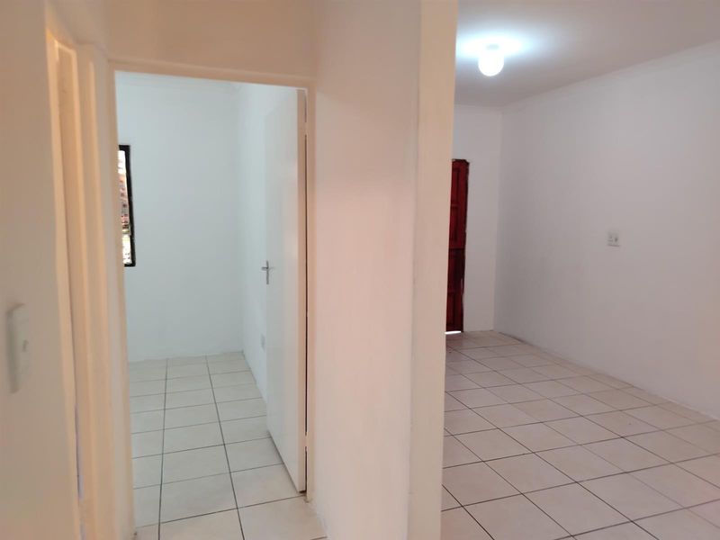 A view through a hallway into adjacent rooms, featuring neutral tiled flooring and simple interior finishes.