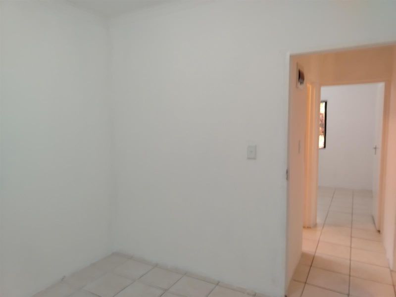 A vacant room with neutral white walls and tiled flooring, featuring a doorway leading into an adjacent hallway.