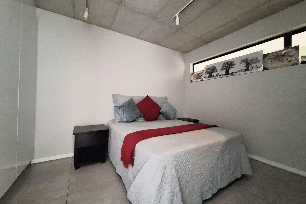 Modern bedroom featuring an exposed concrete ceiling, track lighting, and large format floor tiles with a high-level horizontal window.