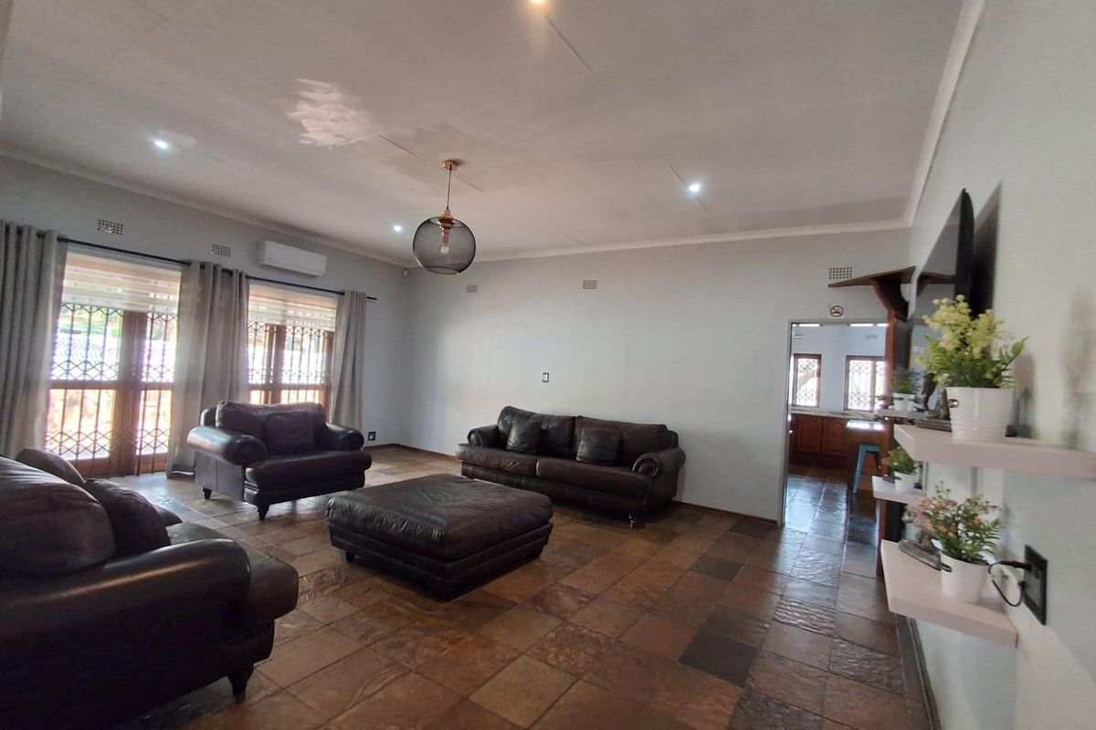 Spacious living room featuring tiled flooring, recessed ceiling lighting, and a wall-mounted air conditioning unit, with direct access to an adjoining kitchen area.