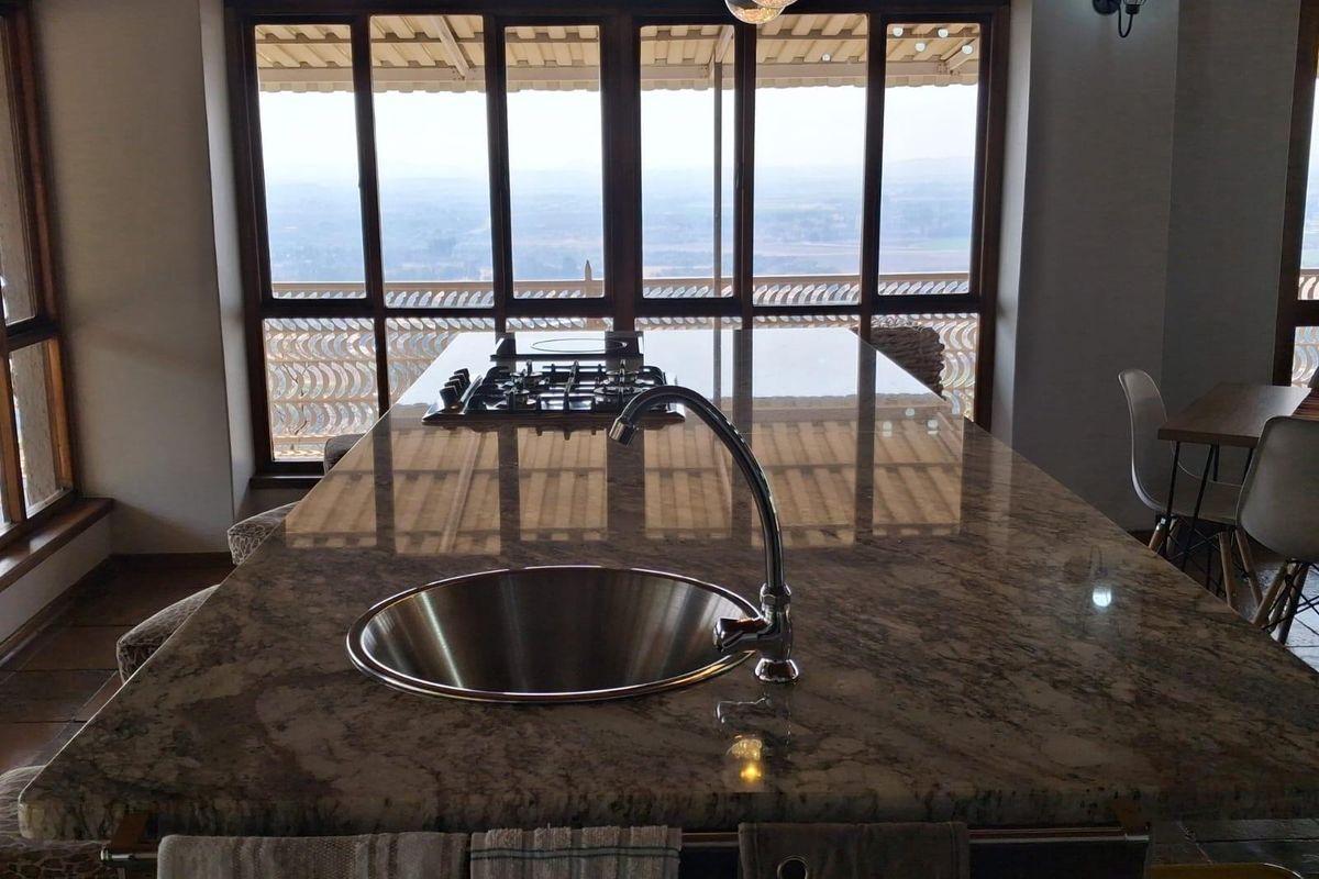 A spacious kitchen island featuring a granite countertop, integrated stainless steel sink, and built-in gas hob, overlooking a scenic outdoor balcony.