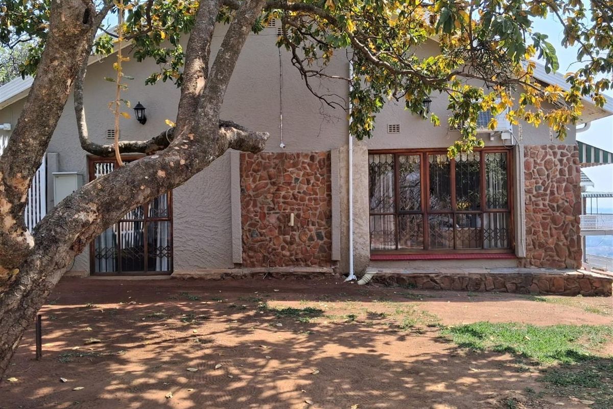 Rear exterior view of the guest house featuring stone cladding accents, large timber-framed windows, and a natural garden setting.
