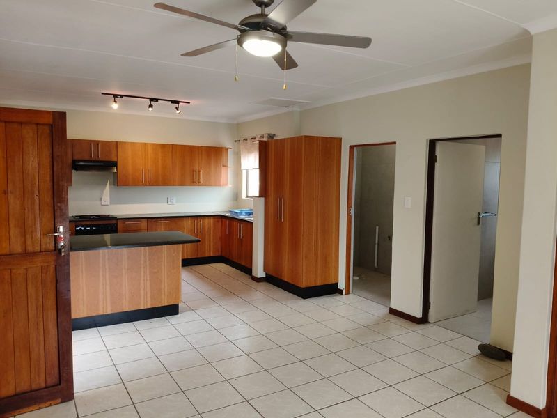 Open plan kitchen featuring wooden cabinetry, granite countertops, and tiled flooring, with adjacent access to utility or bathroom areas.