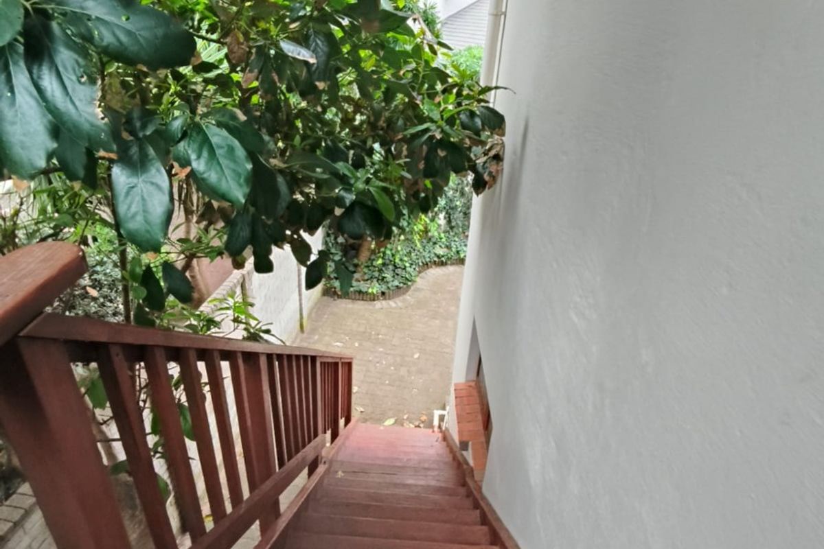 An exterior wooden staircase leading down to a paved rear courtyard area, surrounded by mature foliage.