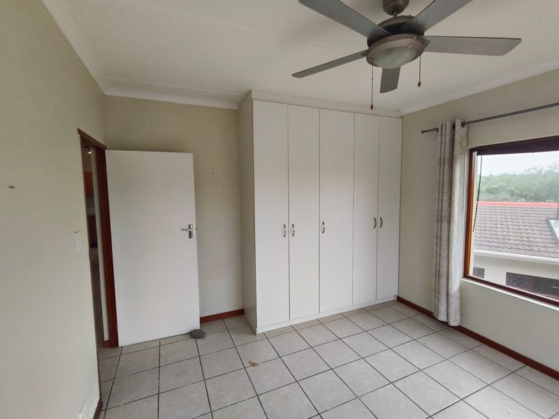 A vacant bedroom featuring tiled flooring, built-in cupboards, and a ceiling fan, offering a clean canvas for personalization.