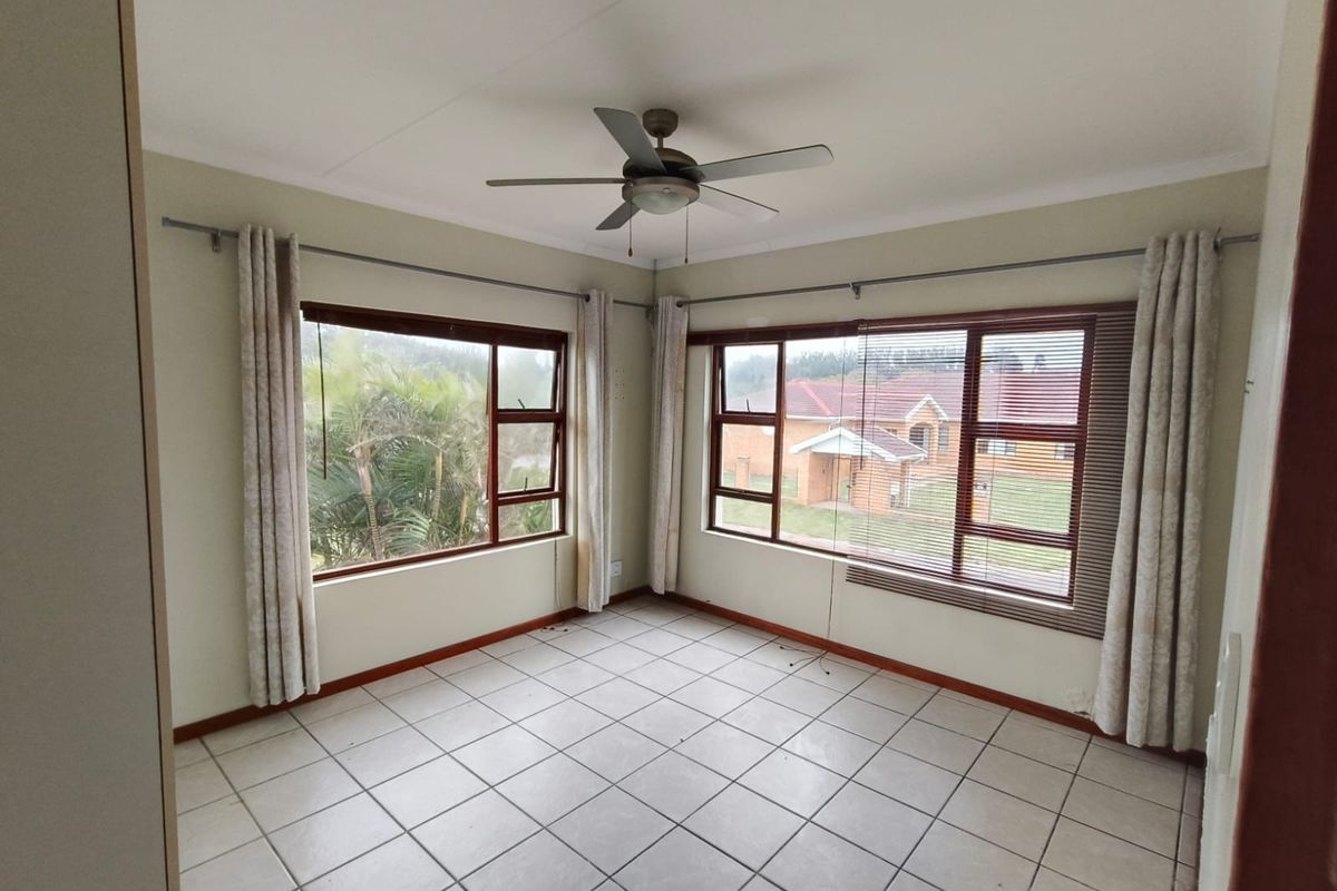 A bright, empty bedroom featuring tiled flooring, a ceiling fan, and large windows with views of the surrounding neighbourhood.