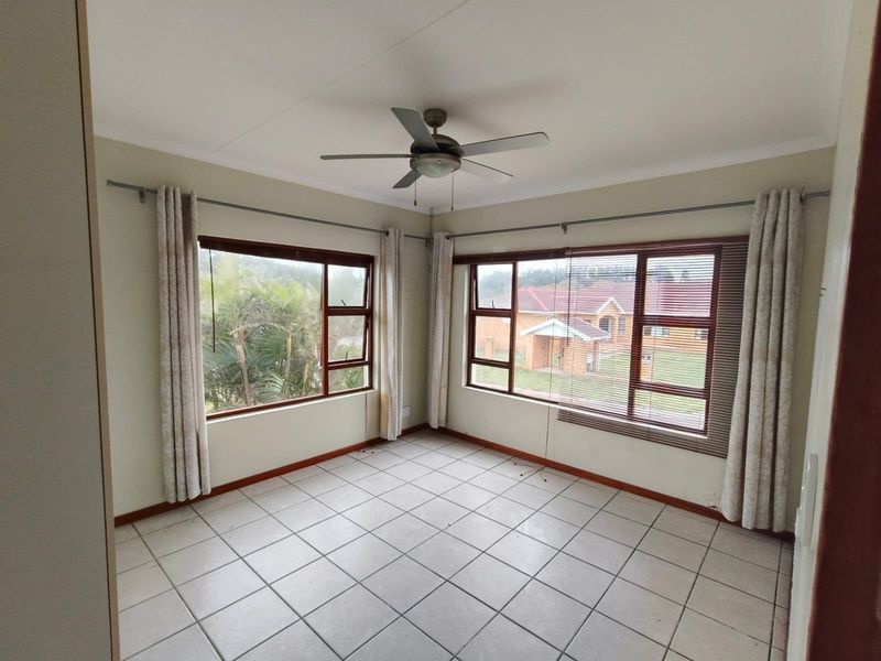 A bright, empty bedroom featuring tiled flooring, a ceiling fan, and large windows with views of the surrounding neighbourhood.