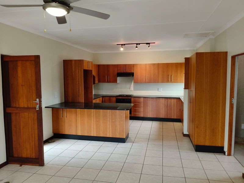 A spacious, empty kitchen featuring warm-toned wooden cabinetry, dark granite countertops, integrated appliances, and neutral tiled flooring, offering a clean and functional layout.