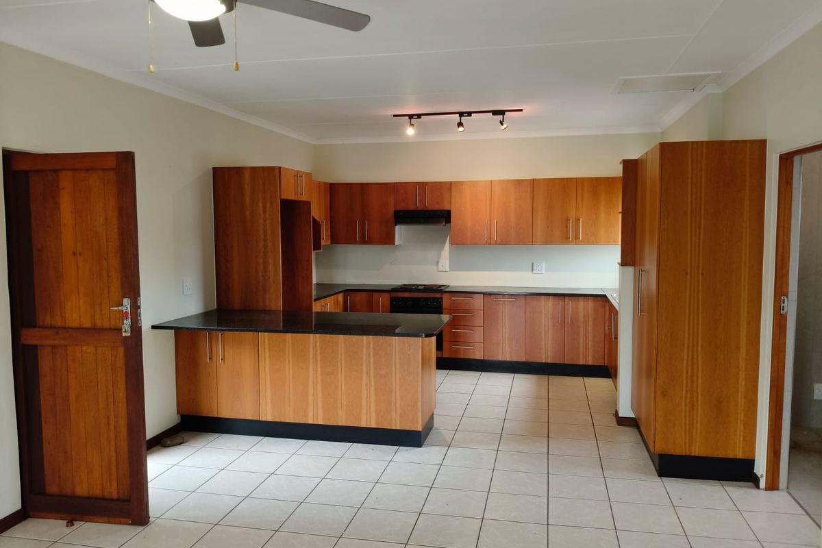 A spacious, empty kitchen featuring warm-toned wooden cabinetry, dark granite countertops, integrated appliances, and neutral tiled flooring, offering a clean and functional layout.