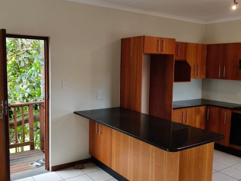 A clean, empty kitchen featuring wooden cabinetry, granite countertops, and a breakfast bar, with direct access to an outdoor balcony area.