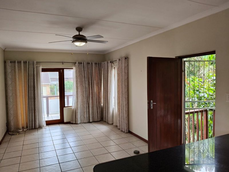 Spacious living area featuring tiled flooring, a ceiling fan, and direct access to an outdoor balcony through sliding glass doors.