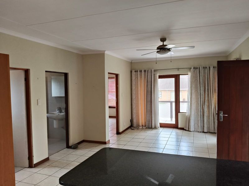 Spacious open-plan living area featuring tiled floors, a ceiling fan, and direct access to a balcony, with an adjacent bathroom visible.