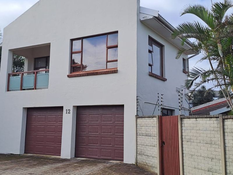 Front elevation of a two-story apartment building featuring a double garage, a private balcony, and secure perimeter walling with electric fencing.