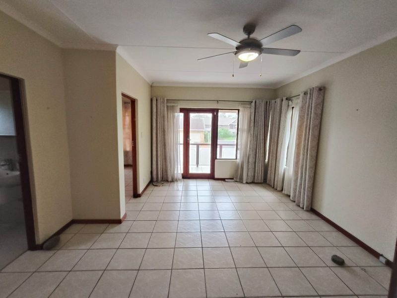 Spacious, tiled living area featuring a ceiling fan and direct access to a balcony through sliding glass doors.