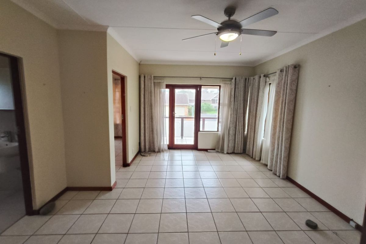 Spacious, tiled living area featuring a ceiling fan and direct access to a balcony through sliding glass doors.