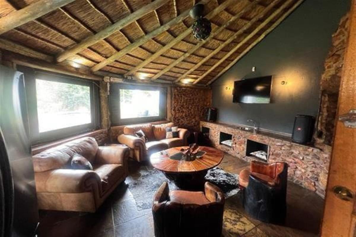Rustic living room featuring a vaulted thatched ceiling, exposed stone wall cladding, and tiled flooring, creating a warm and character-filled entertainment space.