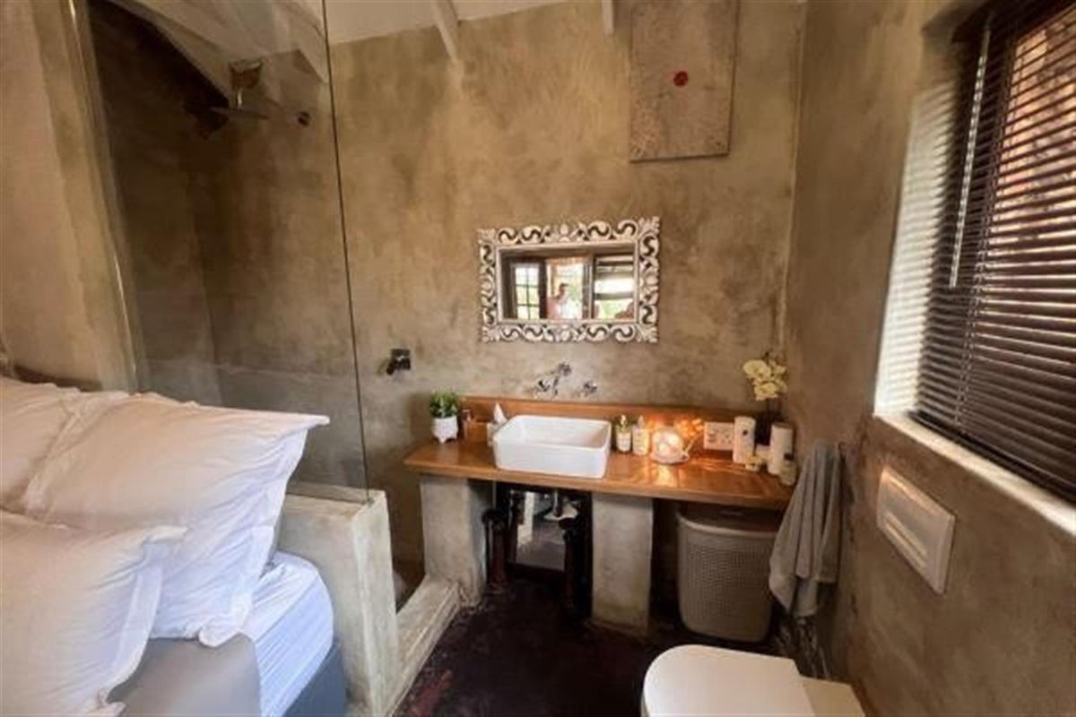 A compact bedroom featuring an integrated open-plan bathroom with a vessel sink, wooden vanity, and glass-enclosed shower area.