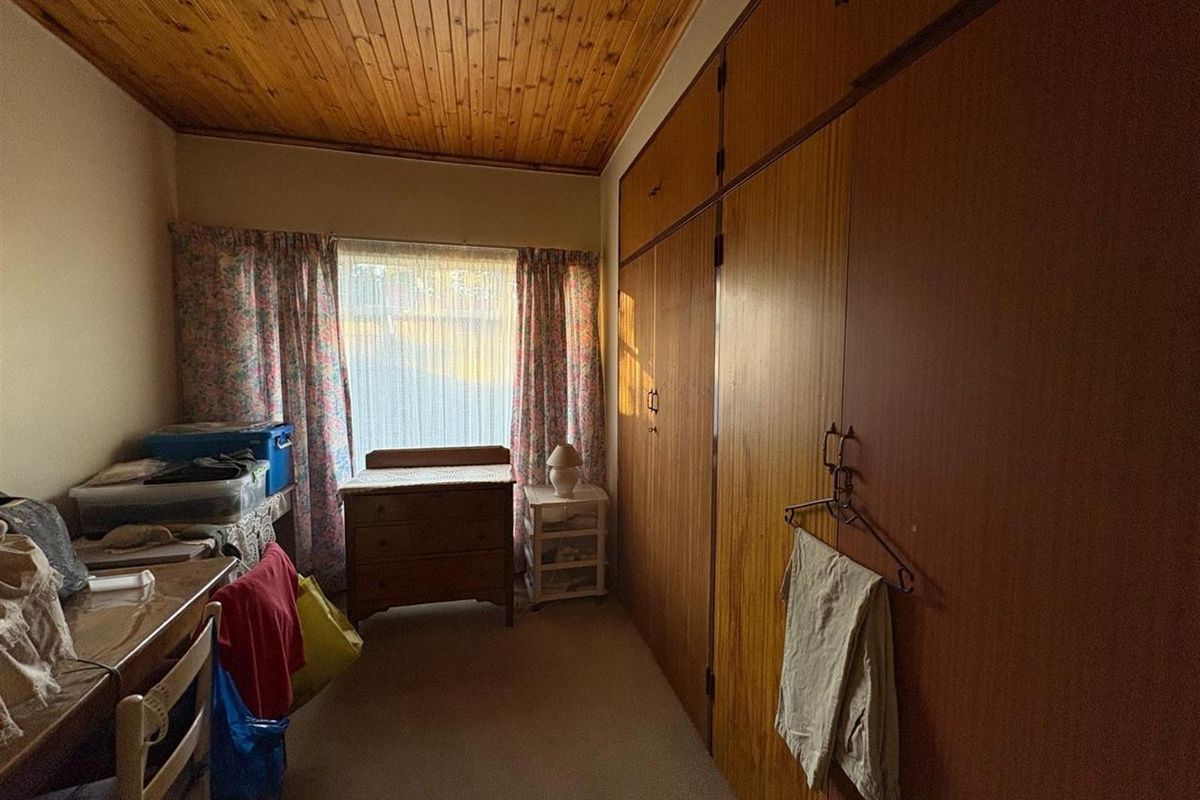 A bedroom featuring dated timber ceiling paneling, wall-to-wall built-in wooden cabinetry, and carpeted flooring.