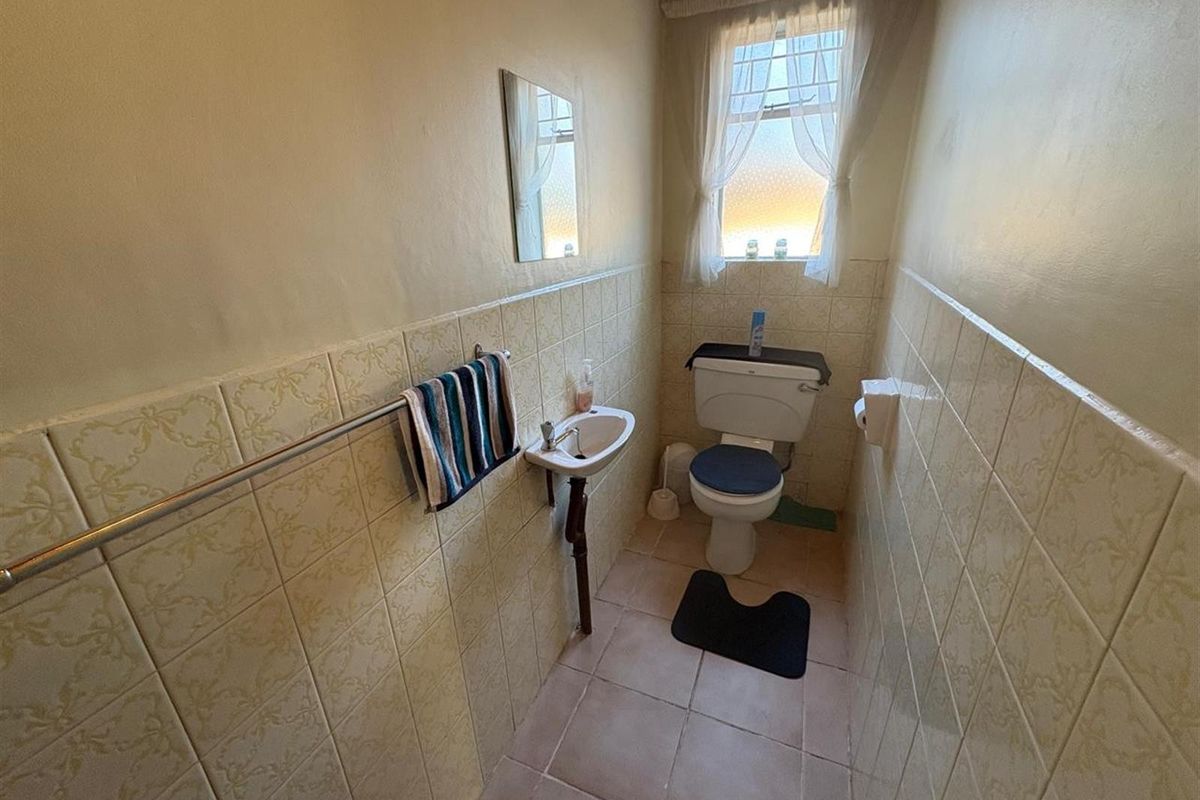 A compact guest bathroom featuring a wall-mounted basin, toilet, and dated ceramic wall tiling.