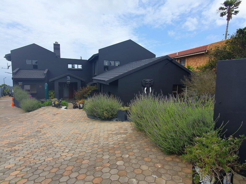 Front elevation of a modern house featuring a dark exterior finish, paved driveway, and landscaped garden area.