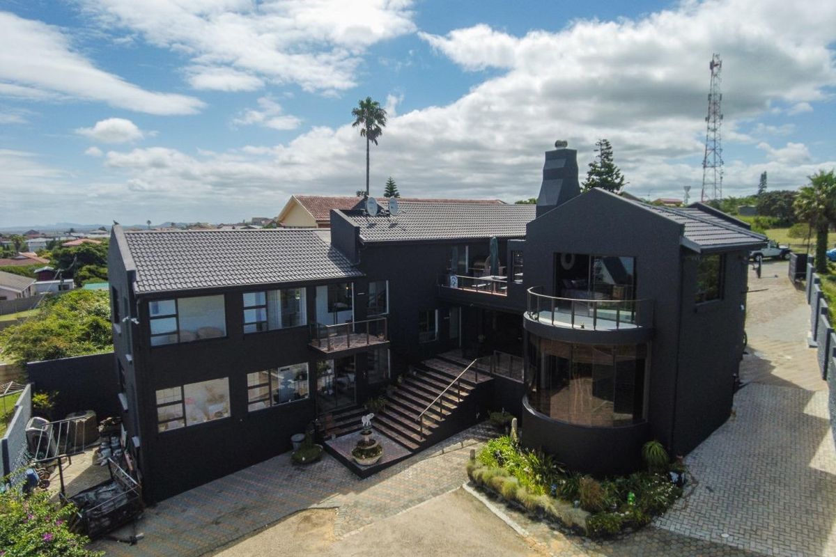 Aerial view of a modern multi-level residential property featuring a dark exterior finish, tiled roof, curved glass architectural elements, and a paved driveway.