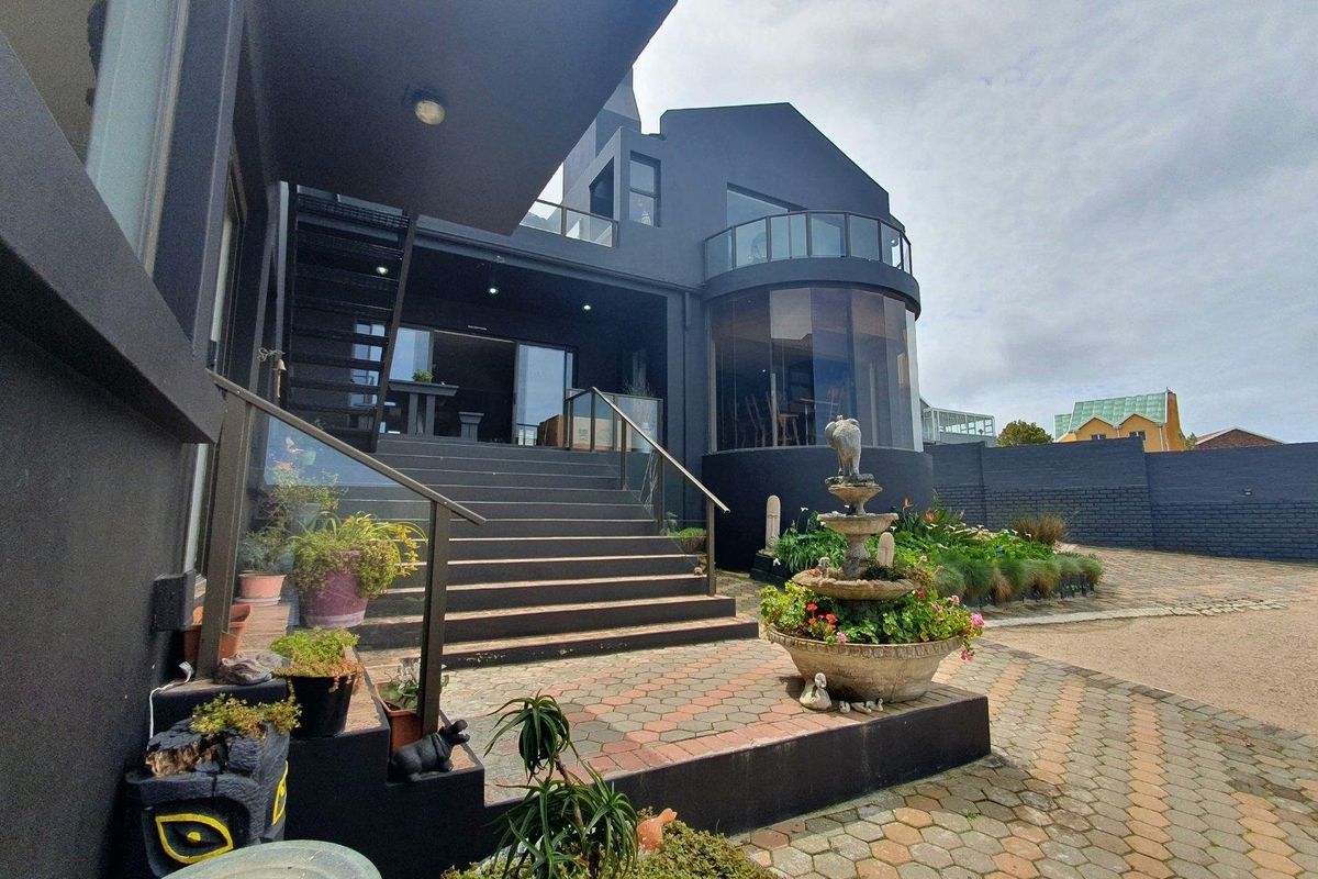 Rear exterior view featuring a modern dark-painted facade, curved glass balcony, paved patio area, and a decorative stone fountain.