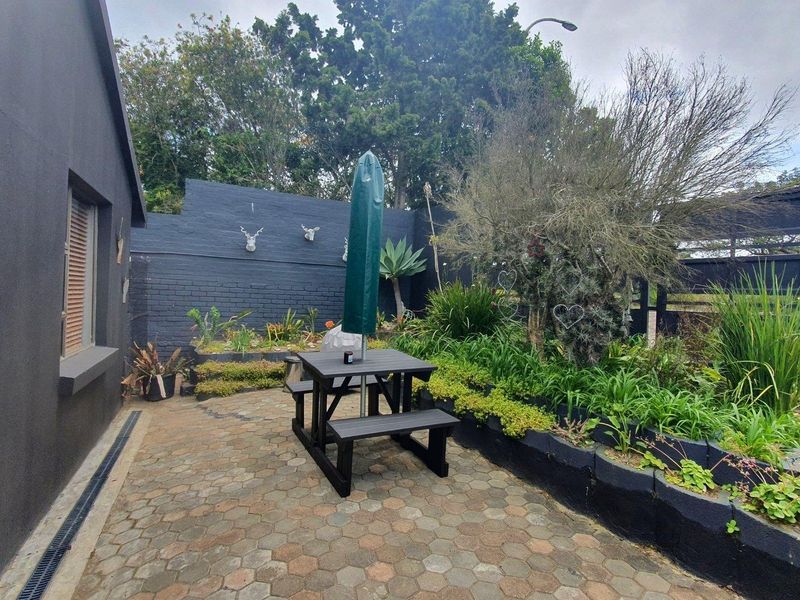 A paved outdoor patio area featuring a retaining wall and established garden beds, providing a private and well-maintained space for outdoor relaxation.