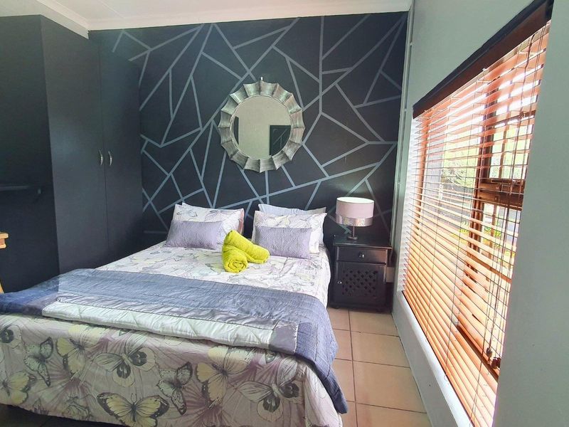 A bedroom featuring tiled flooring, a built-in wardrobe, and venetian blinds, with a decorative accent wall.