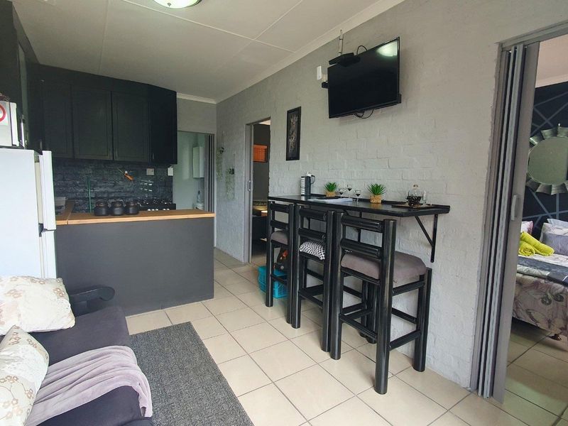 Open-plan living area featuring a compact kitchen with built-in cabinetry, a breakfast bar, and tiled flooring, with direct access to an adjacent bedroom.