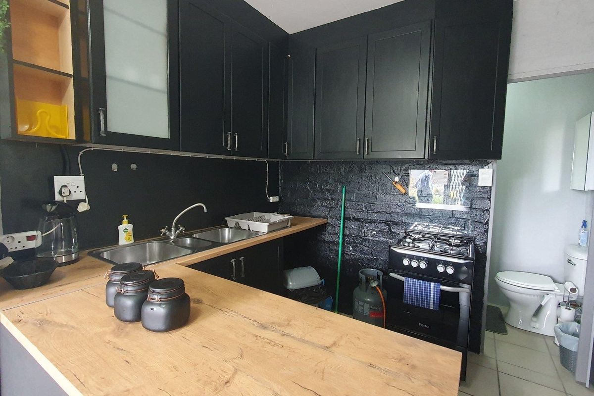 Compact kitchen featuring black cabinetry, wooden countertops, a gas stove, and an exposed brick wall, with an adjacent bathroom visible.